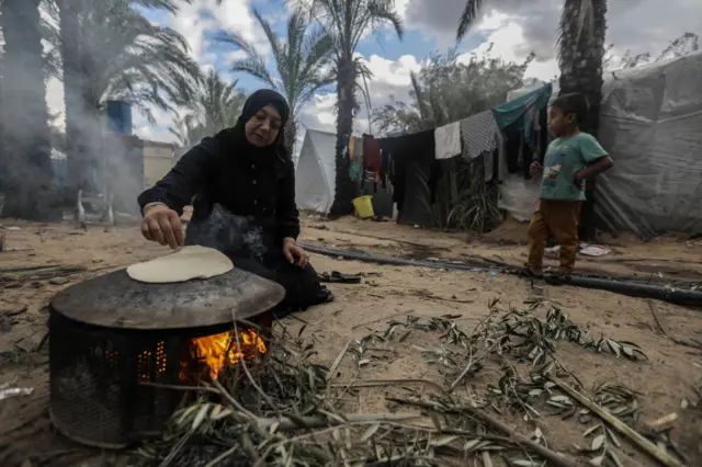 A displaced woman bakes bread over a makeshift stove