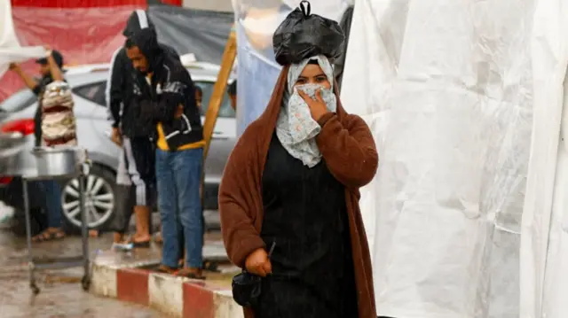 A woman walks under the rain as displaced Palestinians shelter in a tent camp, amid the conflict between Israel and Palestinian Islamist group Hamas, in Khan Younis