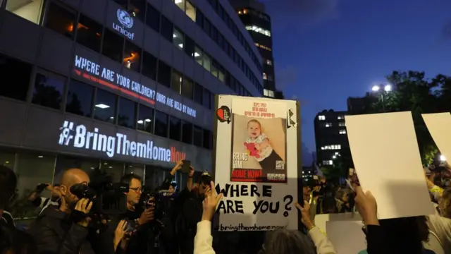 A protester holds a sign with a photo of an infant and the text: "Where are you?"