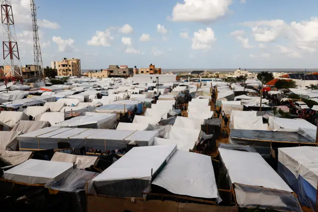 Displaced Palestinian walk in a tent camp in Khan Younis