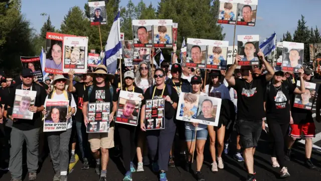 A crowd carrying posters of hostages walk down a street