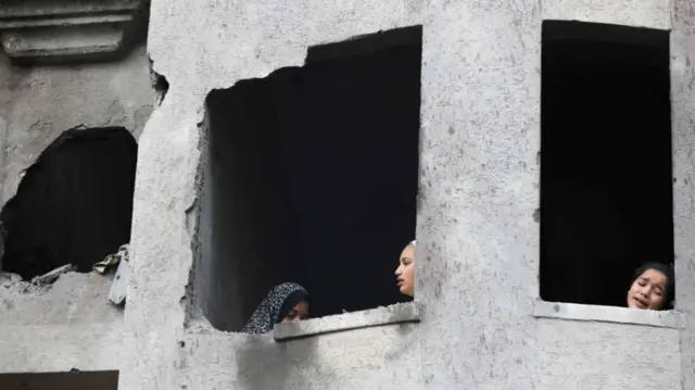 Three young girls looks out damaged windows