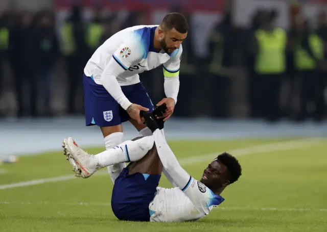 Saka is helped to his feet by Walker.