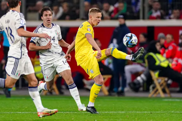 Zinchenko volleys a pass in midfield under pressure from two defenders.