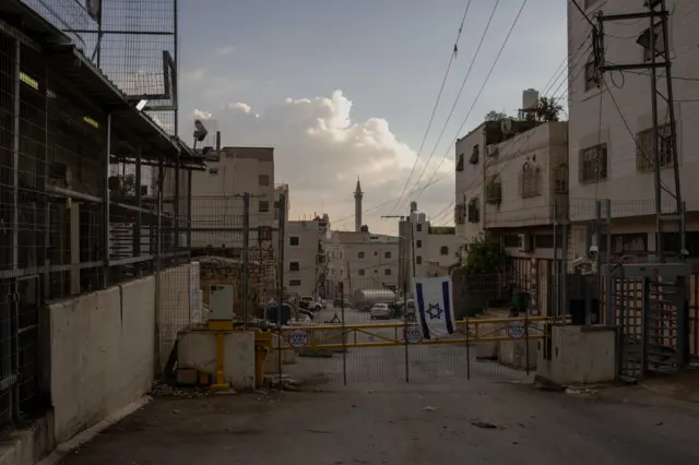 An empty street with a barricade across it, which has an Israeli flag hanging off it