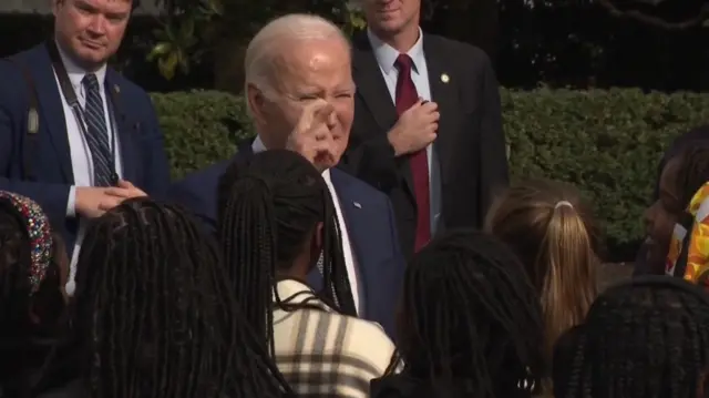 Biden crosses his fingers as he replies to a journalist question at the White House lawn