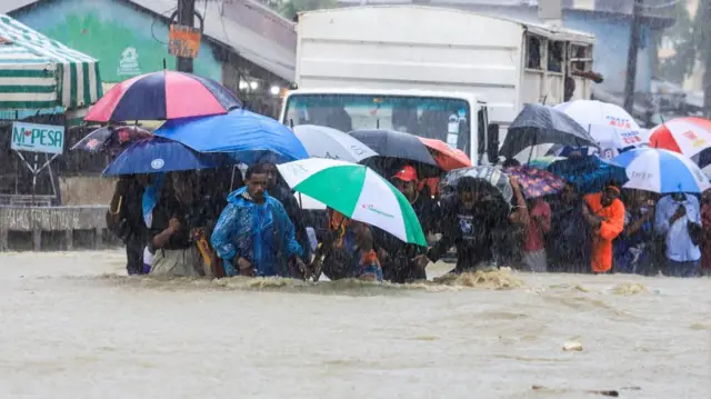 People wade through flood waters along a street following heavy rains in Kisauni district of Mombasa, Kenya November 17, 2023.