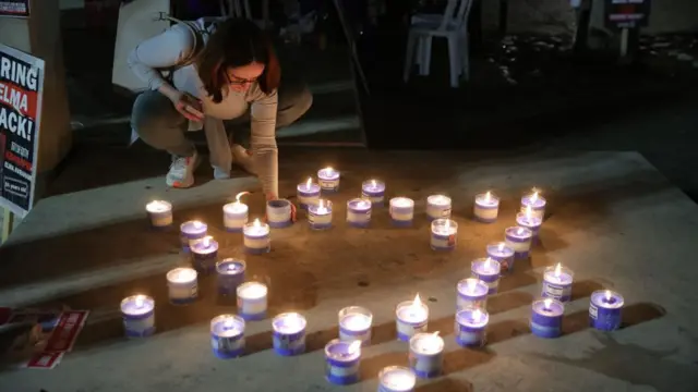 A woman lights a candle which has been placed on the ground as part of a Star of David