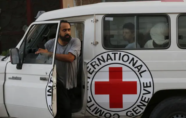 A man climbs out of a vehicle, full of people, which is branded with ICRC livery