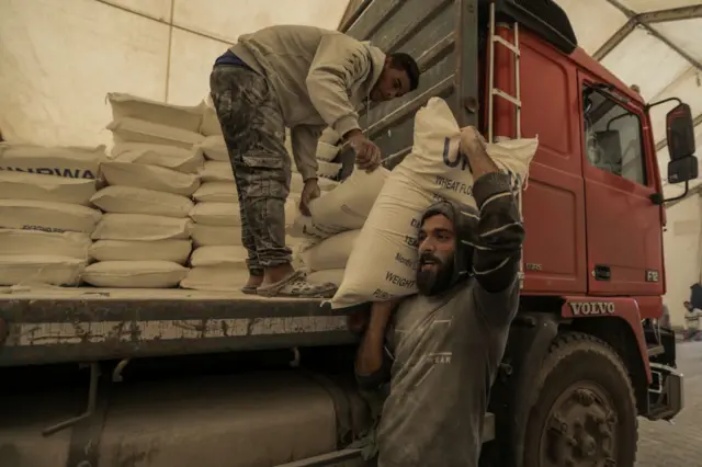 Flour in Unwra-labelled bags is unloaded from a truck by two men