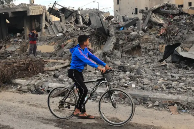 A boy cycles past destroyed buildings