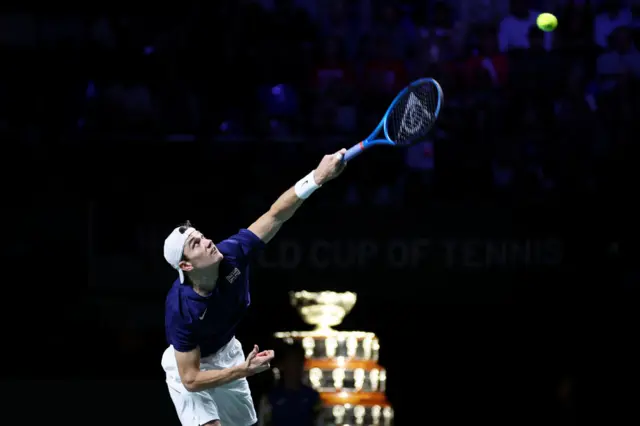 Jack Draper serves with the Davis Cup trophy visible in the background