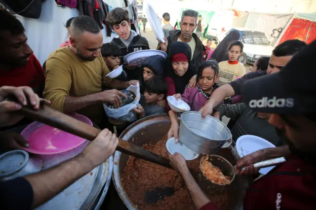 Palestinians are queuing to receive a portion of food on the grounds of the Al-Aqsa Hospital, where they are sheltering in Deir el-Balah, in the central Gaza Strip