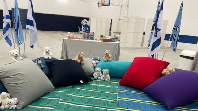 Temporary area for Children in a hostage reception location. There are colourful mats and cushions, stuffed and other toys and Israerli flags