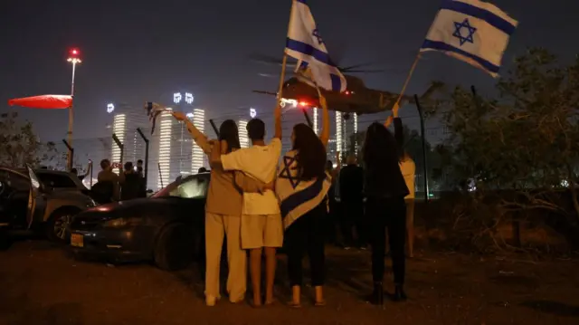 People wave Israeli flags as a helicopter that was carrying hostages released as part of a deal between Israel and Palestinian Islamist group Hamas departures from Schneider Children's Medical Center in Petah Tikva, Israel, November 24, 2023.