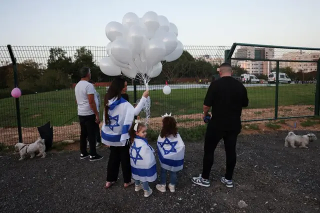 People wait with balloons at the medical centre fence