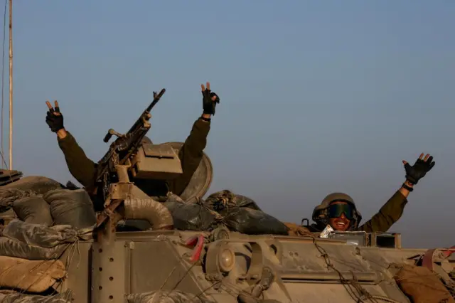 Two soldiers raising their arms from an armoured vehicle