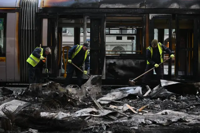 Workers clean up the debris of a burnt train