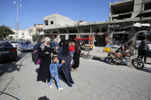 Three women and several children walk along a street in Khan Younis