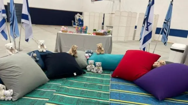 Rugs and pillows arranged on floor of building with teddy bears scattered across them