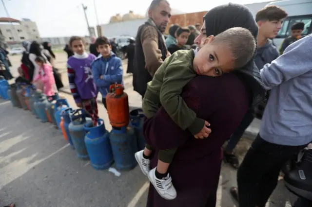 A woman carries a child as Palestinians gather to buy fuel