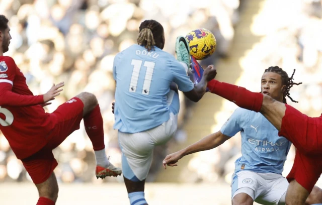 Doku challenges for the ball as Salah kicks it, Ake looks on