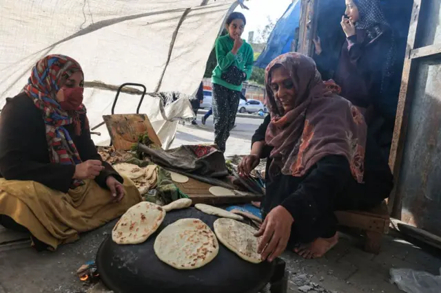 Women bake bread using a makeshift wood stove in Rafah in the southern Gaza Strip on