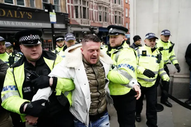 Tommy Robinson is led away by police officers as people take part in a march against antisemitism