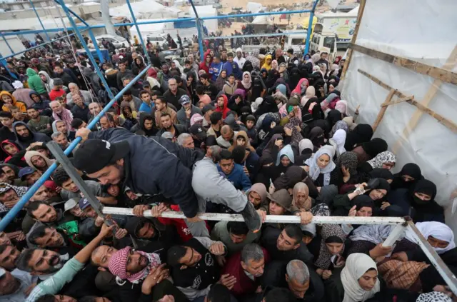 A man climbs on a frame to escape a crowd of people