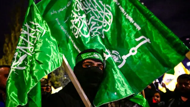 A Palestinian holds Hamas flags while waiting for the release of prisoners in exchange for Israeli hostages held by Hamas, in Ramallah in the occupied West Bank