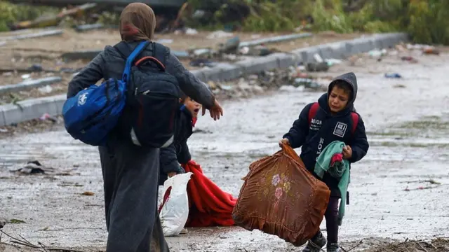 A barefooted Palestinian woman fleeing north Gaza helps her children pick up their belongings as they move southward following rainfall, during a temporary truce between Israel and Hamas, near Gaza City, November 27, 2023.