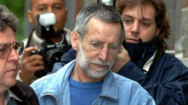 Man looking down surrounded by photographers