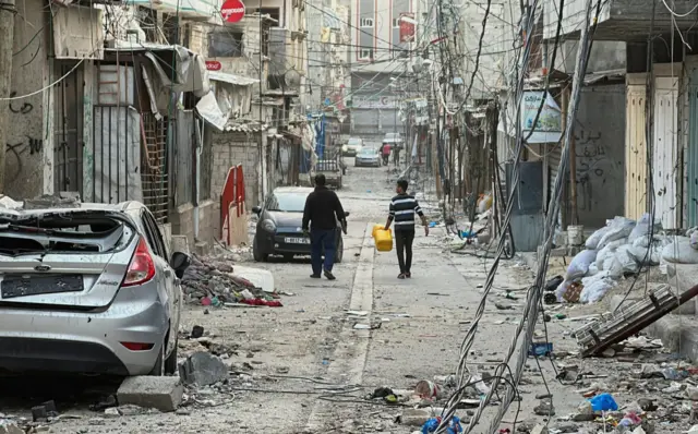 People in Gaza City walk among houses destroyed in Israeli. Photo: 26 November 2023