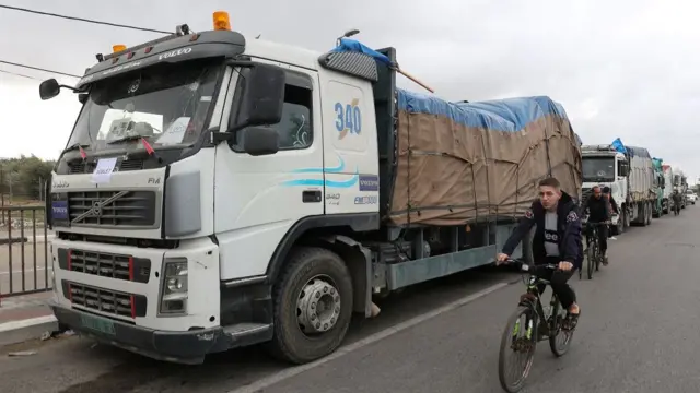 Men ride bikes past trucks carrying aid waiting to head towards north Gaza during a temporary truce between Hamas and Israel, in the central Gaza Strip, November 27, 2023.