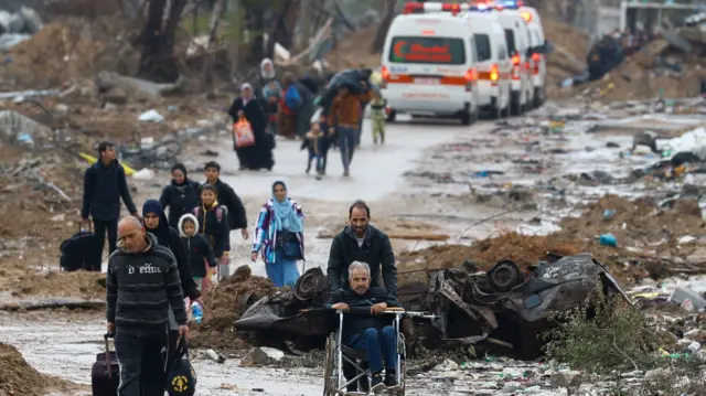 A Palestinian pushes a man in a wheelchair as people fleeing north Gaza move southward, while ambulances head towards the northern part of the territory