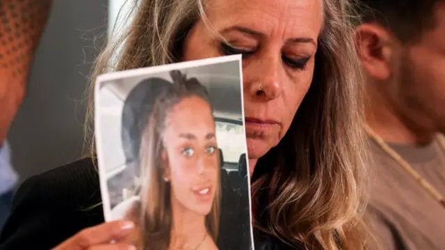 Keren Scharf Schem holding up a picture of her daughter at a press conference in October