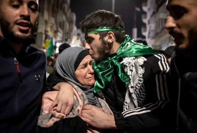 A man wearing a green headband and a green flag as a scarf kisses a woman on the forehead