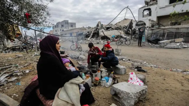 A family sit around a fire next to the remains of their home in Khan Yunis