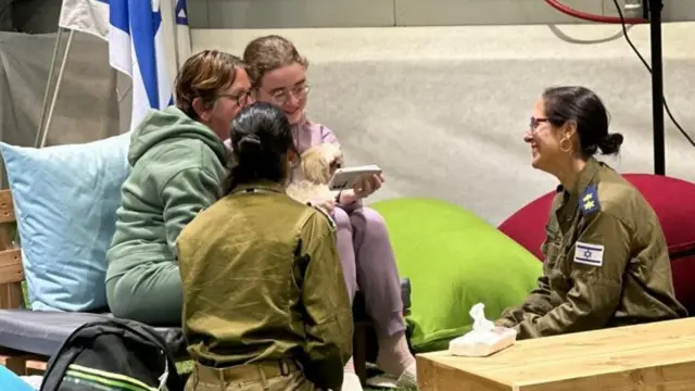 Gabriela and Mia Leimberg hold a phone call with family members, accompanied by two Israeli soldiers