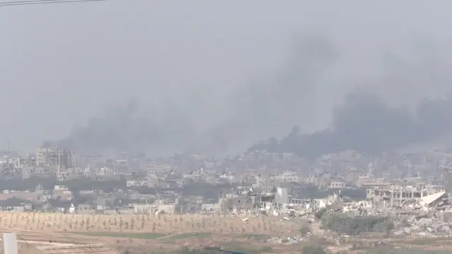 Smoke rises above Gaza as destroyed structures are visible in the foreground