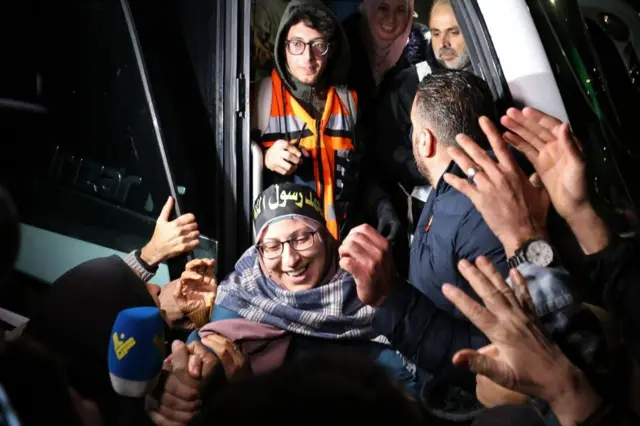 A woman smiles as she gets off a bus and shakes hands