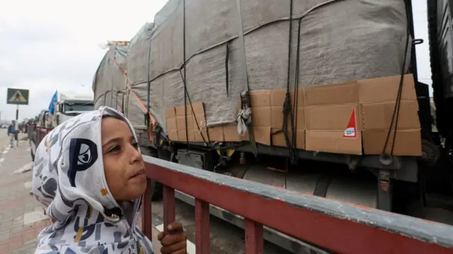 A child looks at trucks carrying aid waiting to head towards north Gaza during a temporary truce between Hamas and in Israel, in the central Gaza Strip, November 27, 2023.