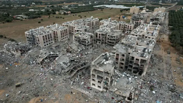 An aerial view of dozens of residental blocks of flats, many of which are 5 stories high, that have been totally destroyed or severely damaged by Israeli airstrikes