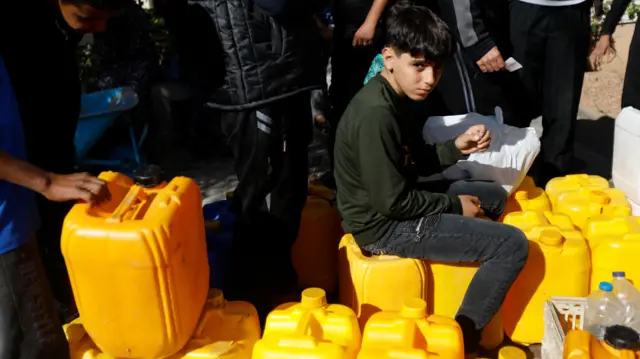 A boy sits on yellow water containers to be filled with water.