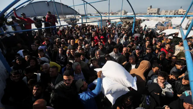 A crowd gathers while white bags of lour are handed out.