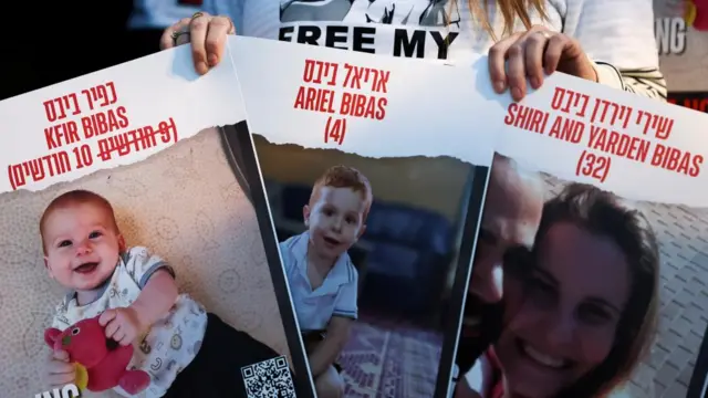 Three posters bearing the faces of Kfir, Ariel, and Shiri and Yarden are held up to the camera