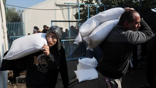 Two Palestinians carry flour bags on their shoulders