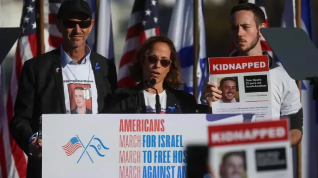 Three people stand on a stage decorated with American and Israeli flags