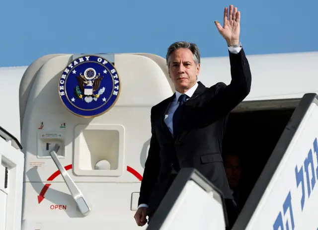 Blinken waves as he departs a plane