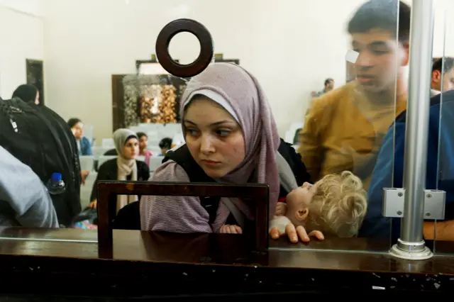 A Palestinian woman holding a foreign passport looks through the counter to get the permission to leave Gaza - 3 November 2023